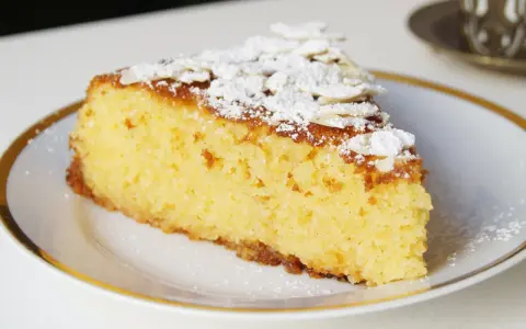 Rebanada de tarta de almendra esponjosa, espolvoreada con azúcar glas y láminas de almendra.