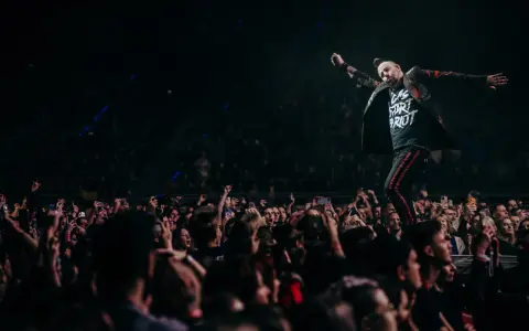 Wokalista Three Days Grace Polska na scenie, z tłumem fanów nagrywających koncert telefonami.