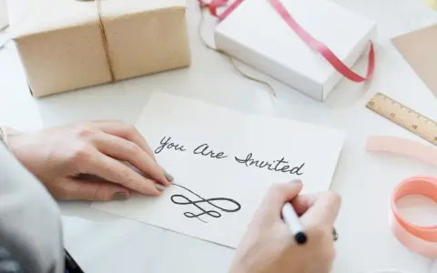 Ręce piszą zaproszenie "You Are Invited". Dowiedz się, jak napisać zaproszenie na urodziny po angielsku.