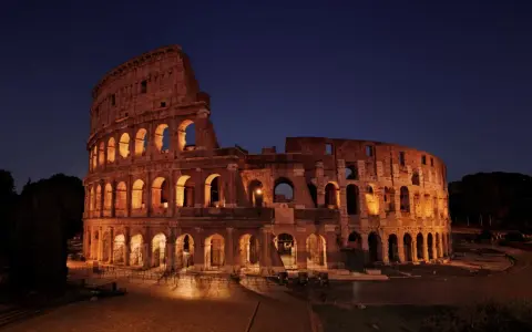 Il Colosseo illuminato di notte, con i suoi archi che creano un gioco di luci e ombre. Ci si chiede perche il Colosseo è bucato, ma la sua storia è scritta nelle sue ferite.