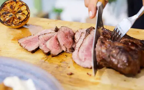 Perfekt grillad ryggbiff skärs upp på en skärbräda. Bredvid ligger en grillad citronhalva.