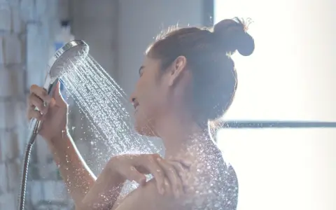 Donna sotto la doccia, l'acqua della doccia esce alternativamente calda e poi fredda, creando un effetto rinfrescante.