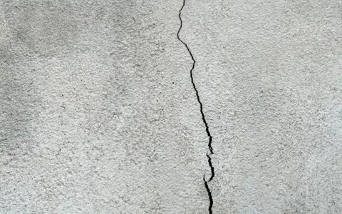 En spricka löper vertikalt över en grov, grå yta, som kan vara en husgrund som behöver putsa.