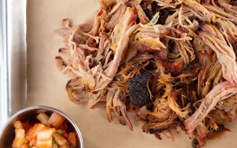 Zartes Pulled Pork, perfekt gegart, zeigt die ideale pulled pork kerntemperatur. Daneben eine Schale mit frischer Salsa.