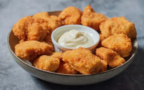 En skål med gyllene, krispiga chicken nuggets och en liten skål med krämig dipp. Perfekt för en snabb och god måltid.