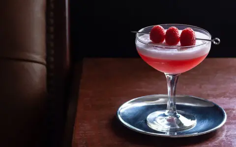 Ein eleganter Clover Club Cocktail mit Himbeeren auf einem silbernen Untersetzer, bereit zum Genuss.