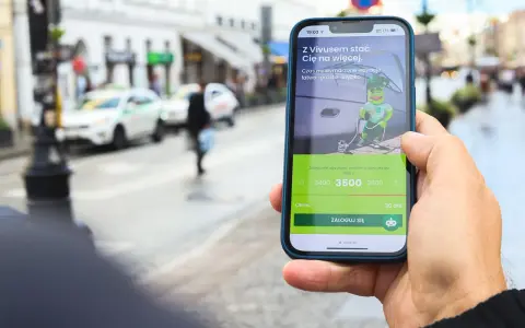 Dłoń trzyma telefon z aplikacją Vivus, gdzie można złożyć wniosek o pożyczkę. W tle miejski krajobraz. Vivus windykacja pomaga spełniać marzenia.