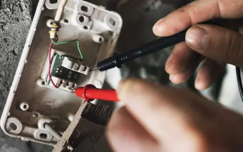 Mains électriques sous tension, un technicien vérifie un fusible qui chauffe avec un multimètre.