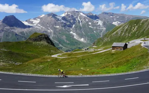Rowerzysta na krętej drodze w Alpach, z majestatycznymi szczytami w tle. To idealne miejsce na podróż szwajcaria motocyklem.