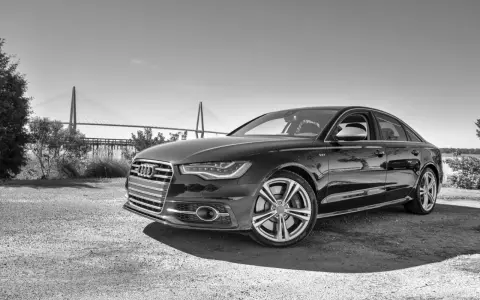 Elegancki czarny Audi S6 C7 z charakterystycznym grillem i felgami, zaparkowany na tle mostu wiszącego.