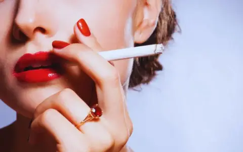 Labios rojos, uñas rojas y un cigarrillo. Una mujer se lleva el cigarrillo a la boca, quizás pensando que la nicotina adelgaza.