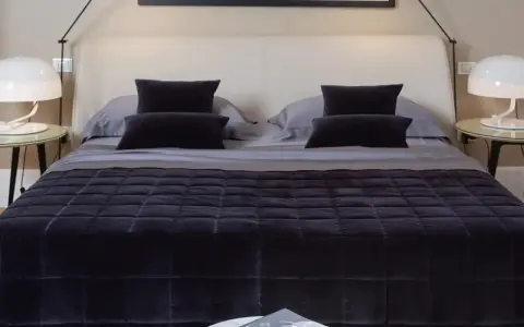 Un letto ben fatto, con copriletto trapuntato scuro e cuscini coordinati. Un esempio di come rifare il letto per un'atmosfera elegante.