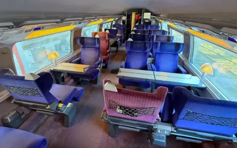 Interior of a bullet train, ready for a journey from Paris to Nice. Plush blue seats with tray tables line the carriage.
