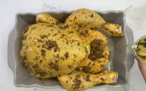 Un pollo al ast, sazonado y listo para hornear, recibe un chorrito de aceite para una cocción perfecta.