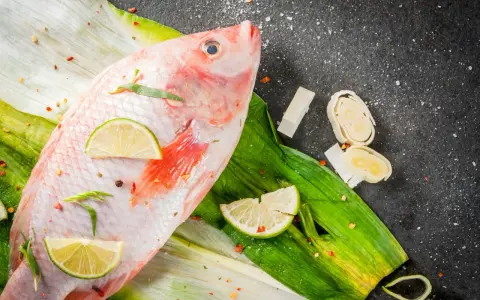 Cała ryba tilapia, przyprawiona chili i limonką, leży na zielonych liściach. Czy to tilapia, co to za ryba?