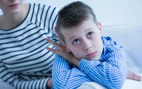 Bambino con sguardo pensieroso, forse durante un test autismo bambini 2 anni. La madre lo osserva con preoccupazione.