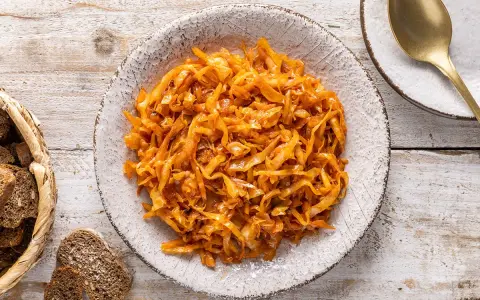 Un saporito cappuccio stufato in padella, servito in un piatto rustico, accompagnato da pane scuro e una posata dorata.