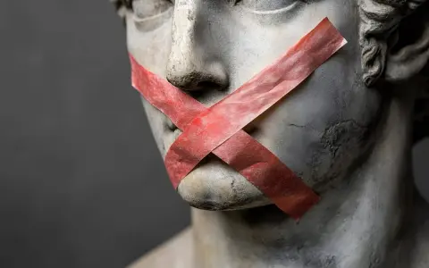 Busto di statua con nastro rosso a X sulla bocca, un esempio di antitesi tra arte e censura.