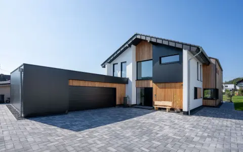Modernes Haus mit Garage, dessen Satteldach modern interpretiert ist. Holz und dunkle Fassadenelemente prägen das Bild.
