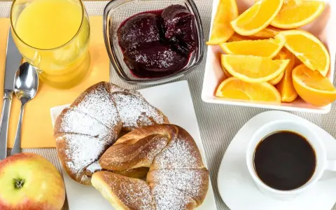 Pyszne śniadanie kontynentalne: rogaliki z cukrem pudrem, pomarańcze, dżem, sok i kawa.