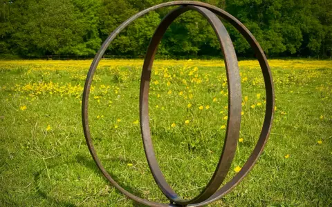 Metallskulptur im Feld mit gelben Blumen. Eine Idee, wie man ein Rondell im Garten gestalten kann, mit rustikalem Charme.