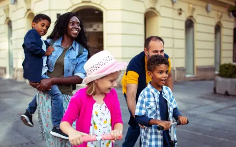 Glückliche Familie unterwegs: Mutter trägt Kind, Vater schiebt Roller. Ein Spagat zwischen Kind und neuem Partner gelingt hier spielerisch.