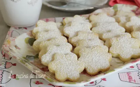 Deliziosi biscotti al burro a forma di fiore, spolverati di zucchero a velo, su un vassoio floreale.