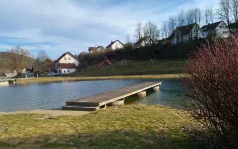Holzsteg am Badesee Forchheim, mit Häusern im Hintergrund und einem Spielplatz.