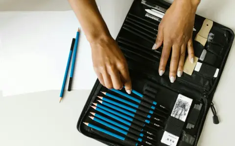 Un étui ouvert révèle une sélection de crayons de différents types pour dessiner, avec des mains choisissant un crayon bleu.