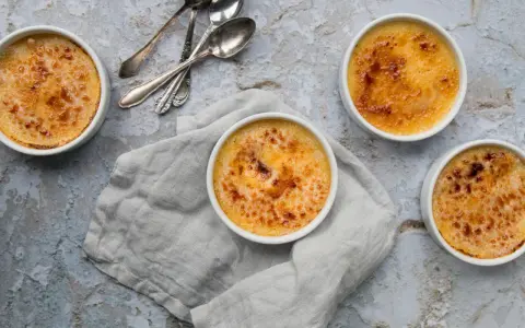 Quatre crèmes brûlées dorées, prêtes à être dégustées. La croûte caramélisée de cette crème catalane invite à la gourmandise.