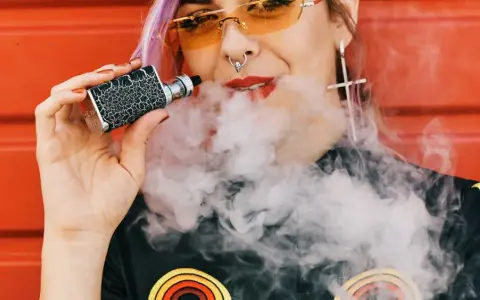 Joven con vaper exhala humo. ¿Cuántas calorías tiene un vaper? La respuesta es cero, ya que no contiene azúcares ni grasas.