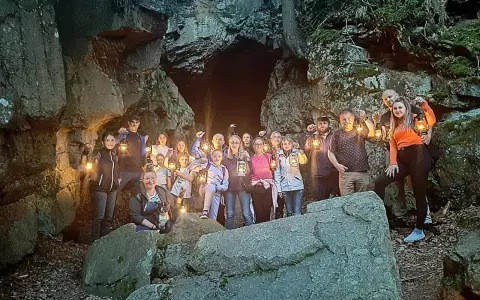 Grupa ludzi z latarniami przy skalnej grocie, odkrywająca tajemnice szlaku walońskiego.