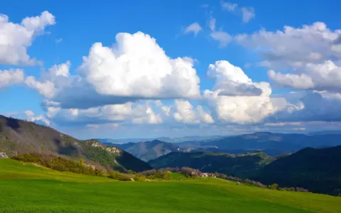 Colli bolognesi cosa vedere: verdi colline, case sparse e un cielo azzurro con nuvole bianche.