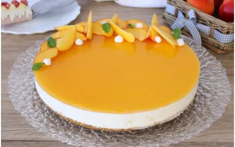 Delizioso cheesecake alle pesche con glassa lucida e fette di pesca fresca, guarnito con menta e piccole meringhe.