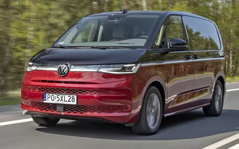 Nowy Volkswagen van w kolorze czerwono-czarnym pędzi po drodze, otoczony zielenią drzew.