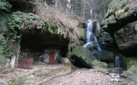 Ein versteckter Wasserfall bei Bad Schandau, mit einer kleinen Höhle und einer roten Tür.