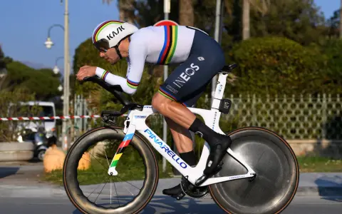 A cyclist in a rainbow jersey races a time trial bike, pushing hard during the Tour de France.