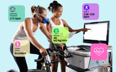 Frau auf Ergometer mit Maske, Trainer überwacht Werte wie VO2max (48 ml/kg/min) und anaeroben Schwellenwert (172 bpm).