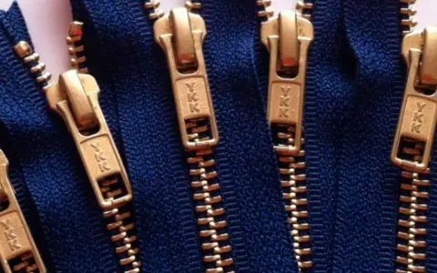 Primer plano de varias partes de una cremallera YKK dorada sobre tela azul.