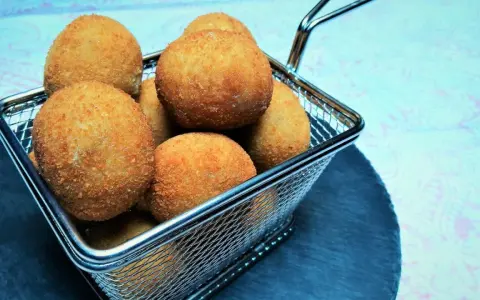 Croquetas doradas y crujientes en una cesta metálica.