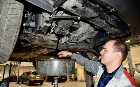 Mechanik spuszcza olej z silnika samochodu. Regularna wymiana oleju to klucz do długowieczności auta.