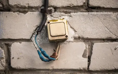Interrupteur électrique beige en saillie sur un mur de briques, fils dénudés bleus et blancs.