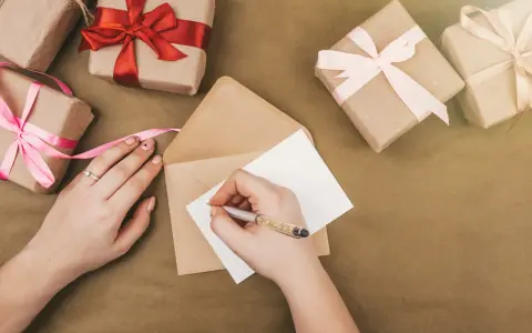 Piszę kartkę z podziękowaniem za zaproszenie na imprezę. Wokół leżą prezenty owinięte w papier i ozdobione wstążkami.