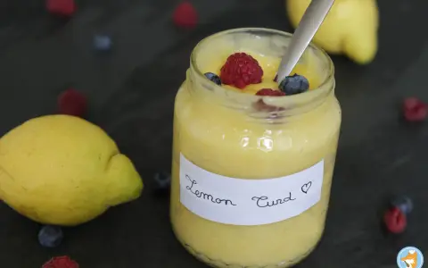 Un pot de lemon curd maison, garni de framboises et myrtilles, avec des citrons frais et des baies éparpillés.