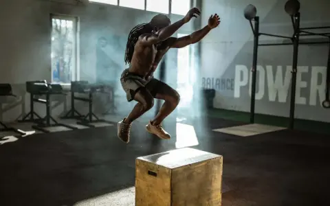 Mann mit Dreadlocks macht explosive Box Jumps in einem nebeligen Fitnessstudio.