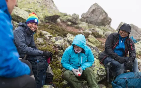 Vänner vilar på berg i snöfall, deras impregnerade jackor håller dem torra.