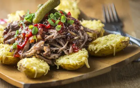 Pulled pork med en härlig sås till, serverad med ugnsbakade potatishalvor gratinerade med ost och en dillkvist.