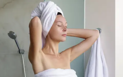 Frau mit Handtuch auf dem Kopf, nach dem Duschen. Sie denkt darüber nach, wie man Reiswasser für die Haarpflege macht.