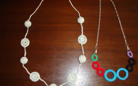 Dos collares de ganchillo y abalorios: uno blanco con esferas y círculos calados, y otro con cadena plateada y aros de colores.