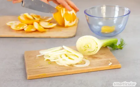 Frischer Fenchelsalat wird zubereitet. Eine Person schneidet Orangen, während Fenchelscheiben auf einem Holzbrett liegen.